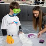 Female Randolph student teaches a science experiment to a young boy.