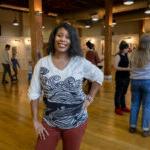 Michelline Hall poses in the middle of an art gallery, with her hand on her hip