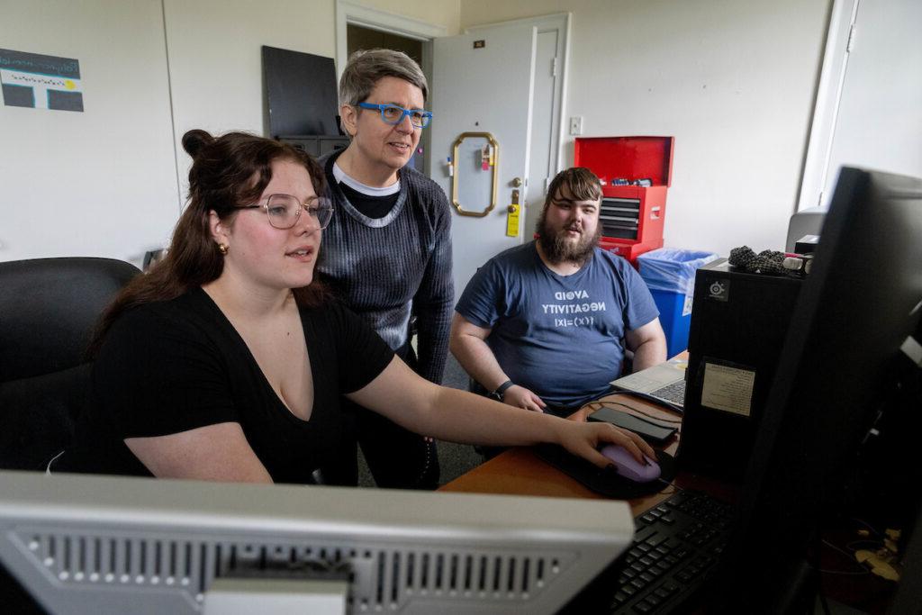 Luke Chapman and Shauna Shepard sit at a computer, with professor Katrin Schenk sitting behind them