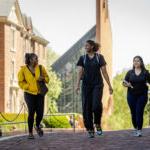 Three students walk on back campus, with the chapel in the distance behind them